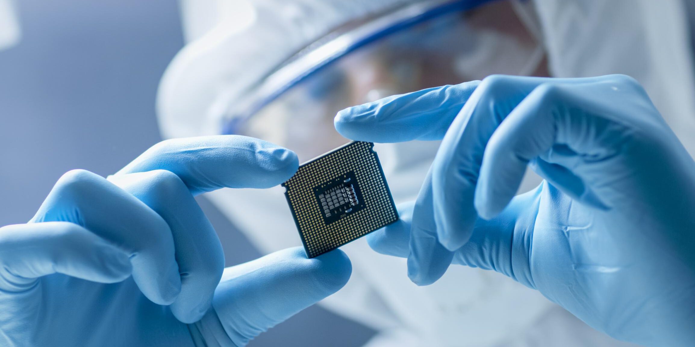 In Ultra Modern Electronic Manufacturing Factory Design Engineer in Sterile Coverall Holds Microchip with Gloves and Examines it.